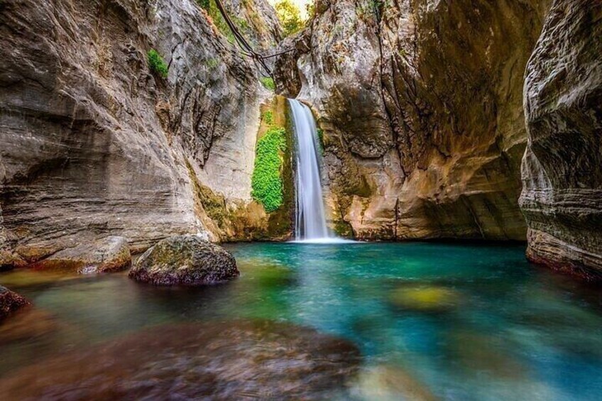 A waterfall in a rocky canyon with clear water and green vegetation. 1