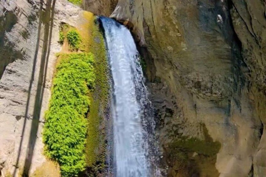 A waterfall cascading down a rocky cliff with lush green vegetation at its base. 4
