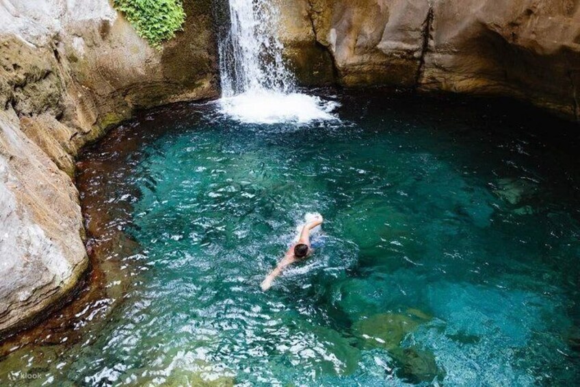 A person swimming in a clear blue pool with a waterfall above. 5
