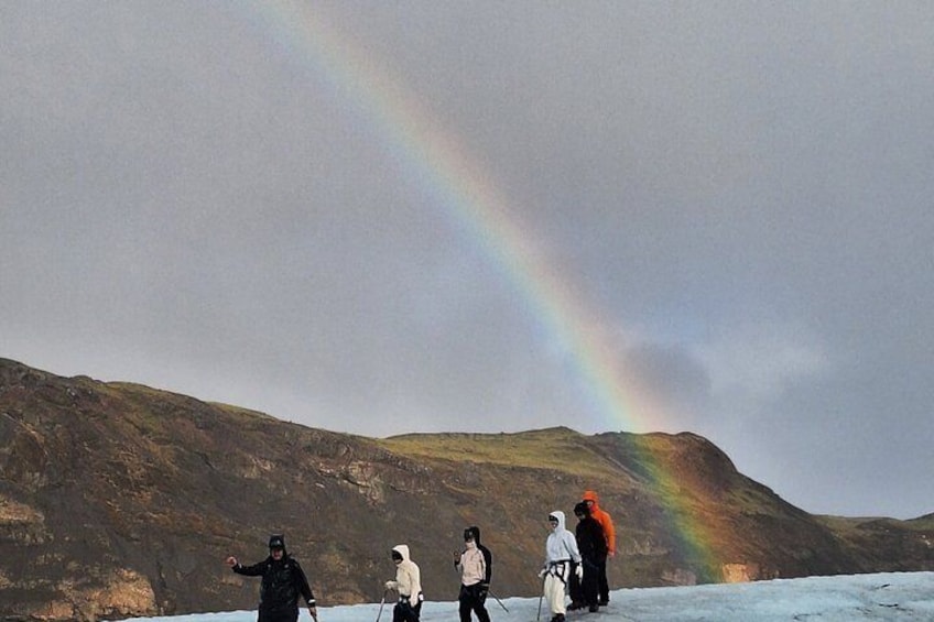 A group of people standing on a snowy landscape with a rainbow in the sky. 5
