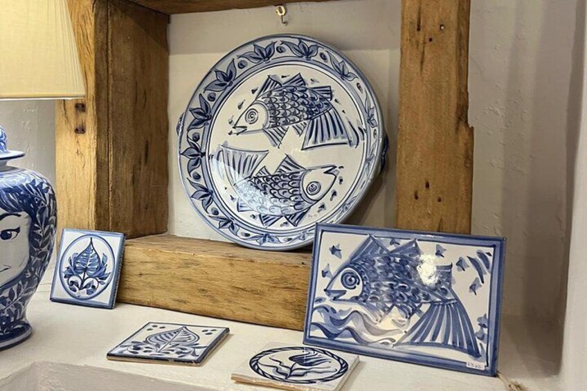 Une collection de carreaux de céramique bleus et blancs ornés de motifs de poissons et de fleurs, exposés sur une étagère en bois. 2