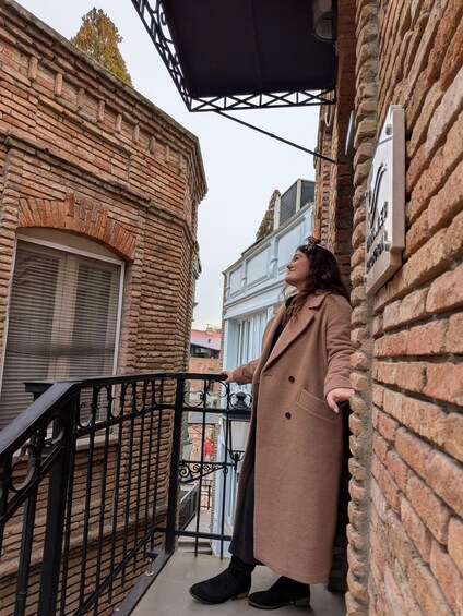 A person standing on a balcony with a brick wall and a metal railing. 2