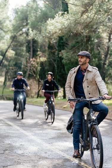 Three cyclists on a paved path surrounded by trees. 1