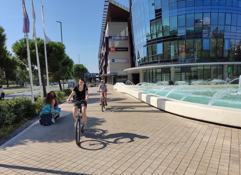 A paved bike path with cyclists, a modern building with glass facade, and a water feature. 3