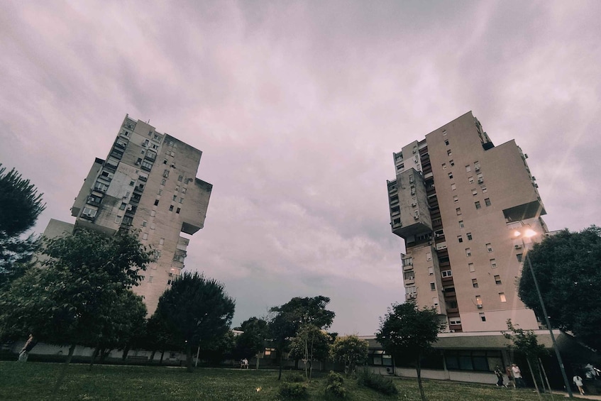 Two tall residential buildings with balconies, surrounded by trees and a grassy area. 4