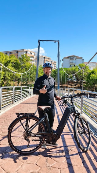 A person standing next to a bicycle on a bridge with metal railings and trees in the background. 2