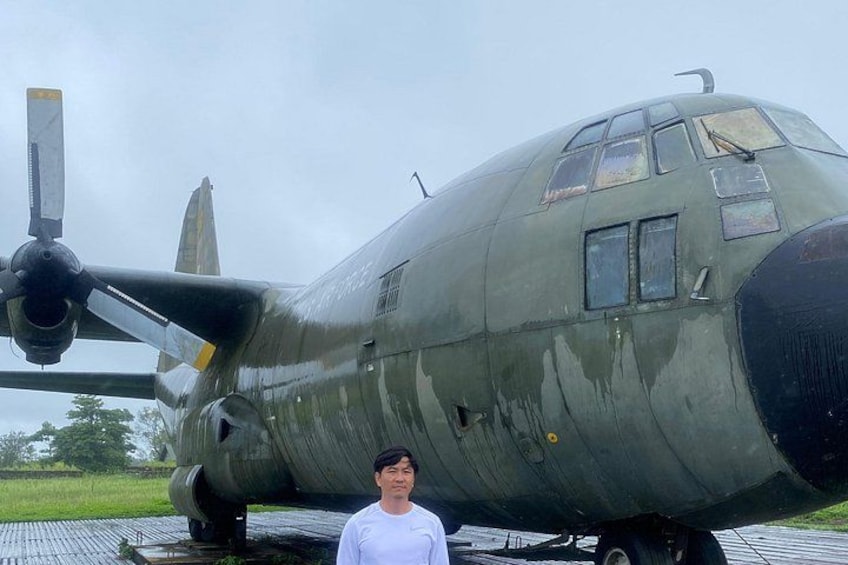 Ett militärflygplan med en propeller, en person som står framför det, och ett gräsbevuxet fält i bakgrunden. 5