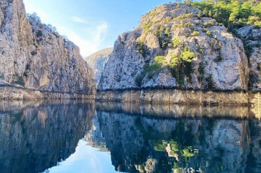 A calm lake with rocky cliffs and trees reflecting in the water. 1