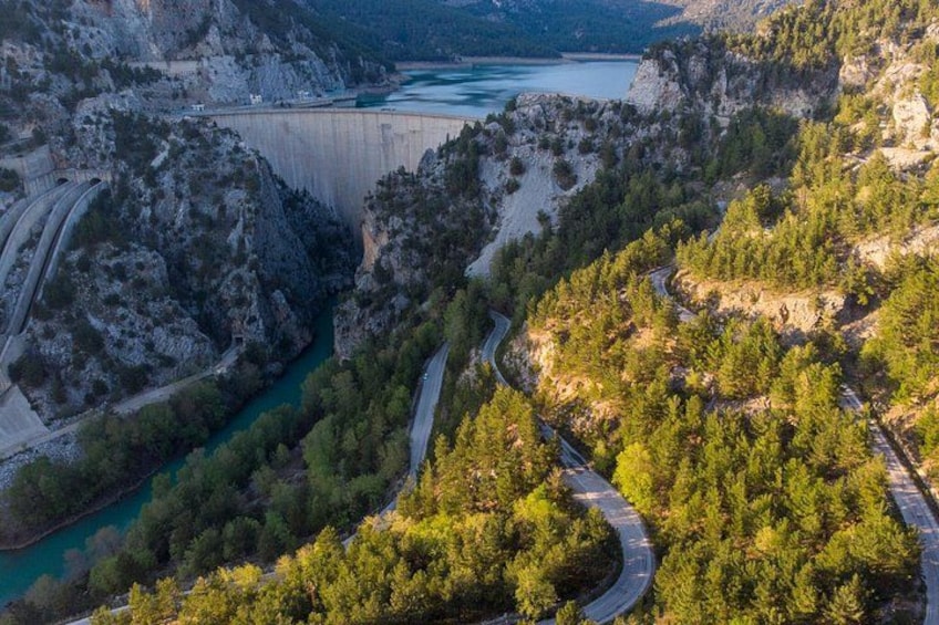 A mountainous landscape with winding roads, a river, and a large dam. 2