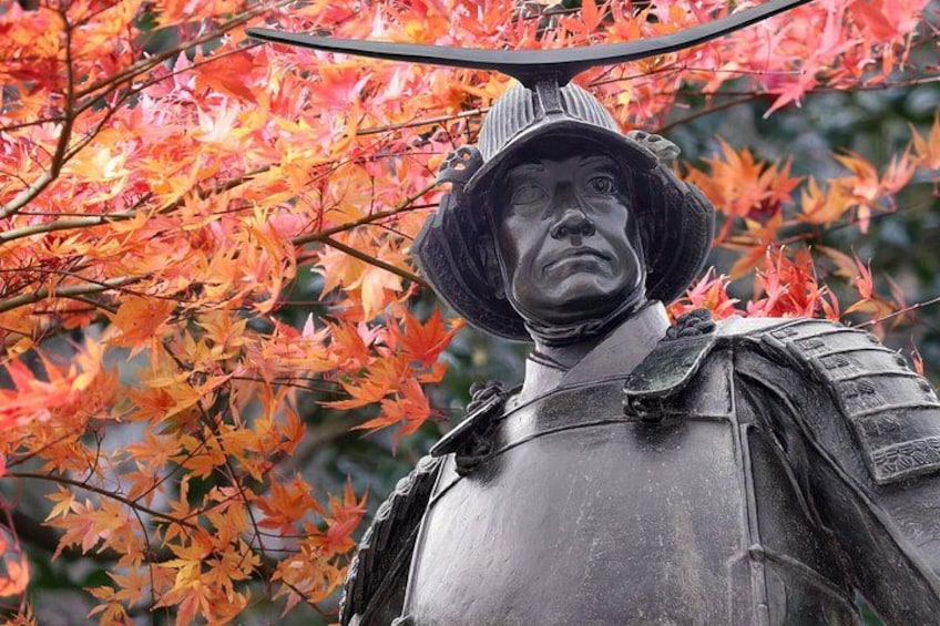 A statue of a historical figure with a hat and armor, surrounded by autumn leaves. 4