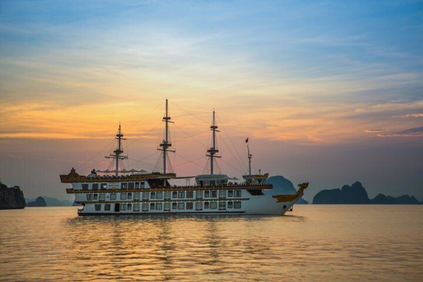 A large, multi-deck boat with multiple masts sailing on calm waters during sunset. 1