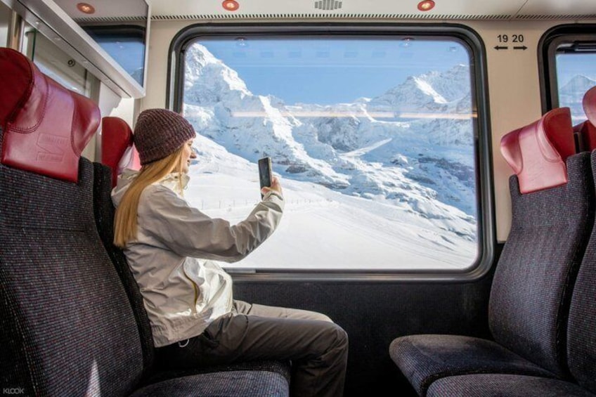 A person taking a photo of a snowy mountain landscape through a train window. 5