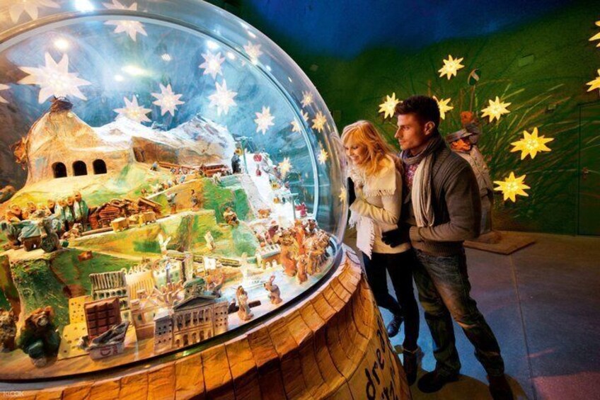 A glass dome with a miniature village scene, a wooden base, and star decorations. 2