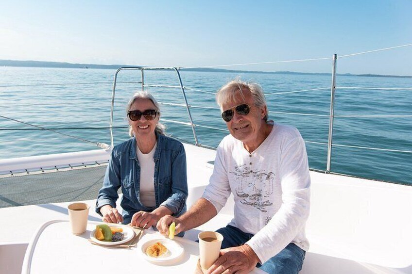 Two people on a boat with a table, food, and drinks. 4