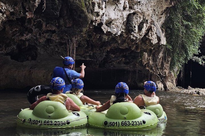 People rafting in green inflatable boats with helmets, navigating a river with a rocky cave backdrop. 4