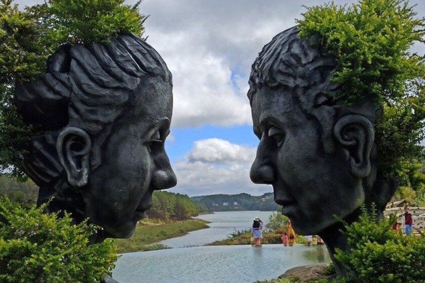 A sculpture of two heads facing each other with a river and mountains in the background. 3