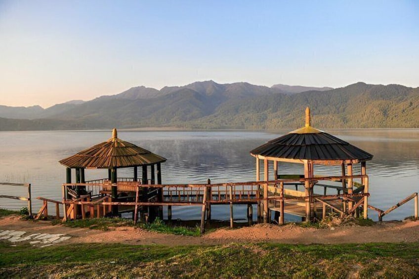 Two wooden gazebos on a lakeside platform with mountains in the background. 4