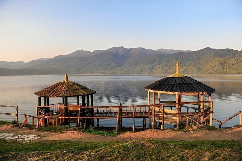 Two wooden gazebos on a lakeside with mountains in the background. 4