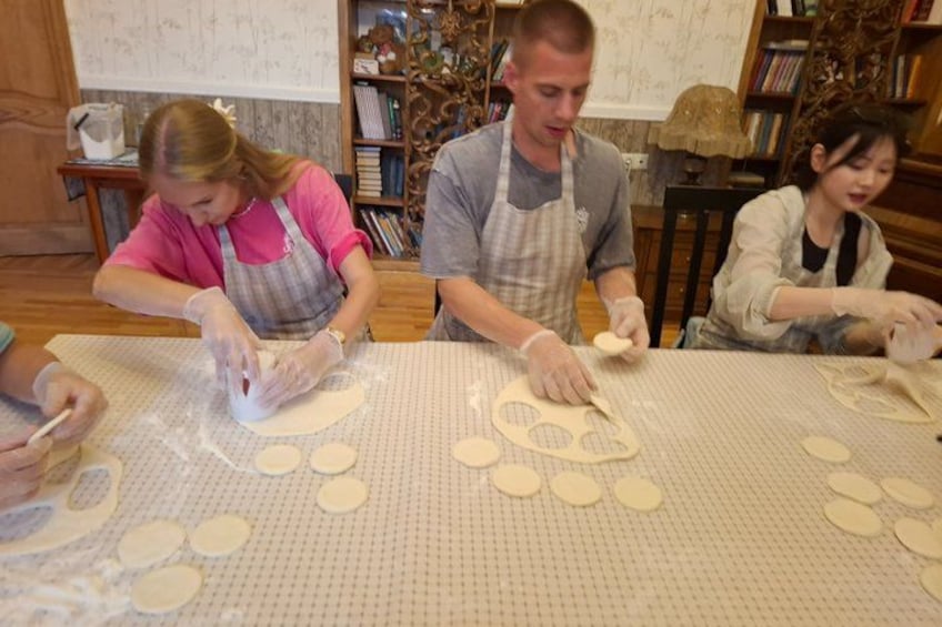 People working with dough on a table, surrounded by books and decorative items. 4