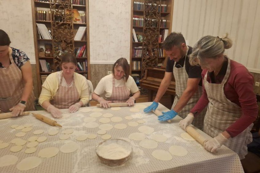 A group of people rolling out dough on a table with a rolling pin and a bowl of flour. 2