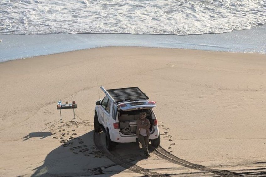Un SUV blanco estacionado en una playa arenosa, con huellas que conducen hasta él. 4
