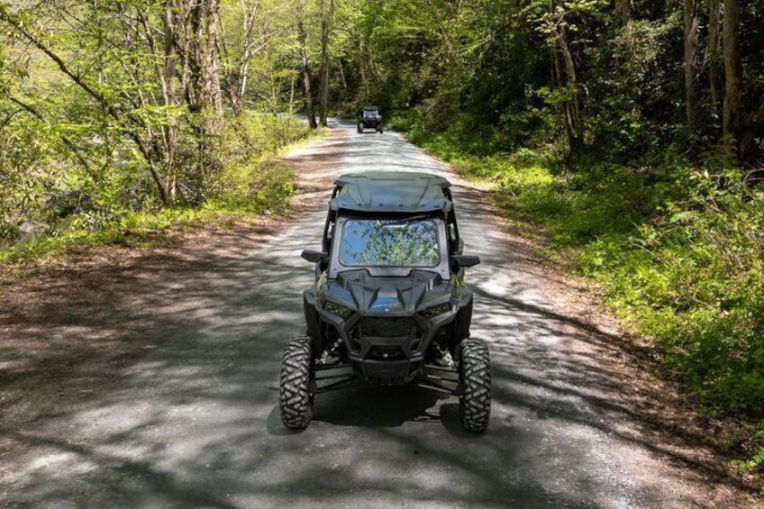 A black ATV on a forested road with a vehicle ahead. 4
