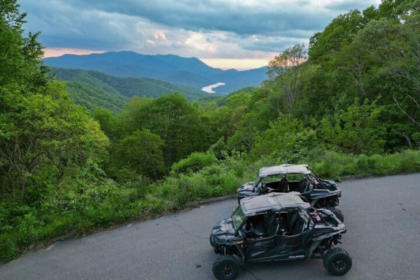 A black off-road vehicle on a paved road surrounded by lush greenery and mountains in the background. 2