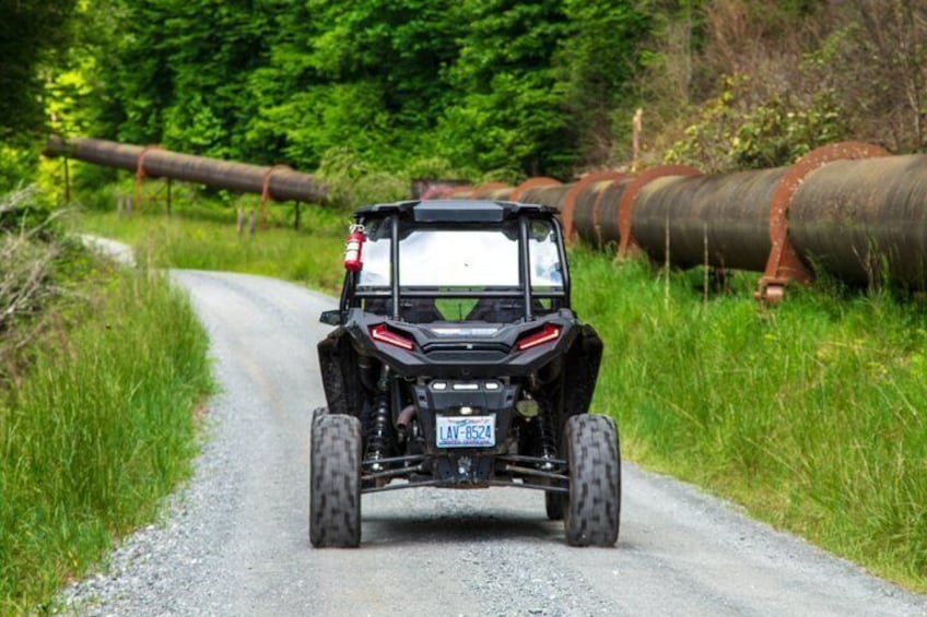 A black off-road vehicle on a gravel road with a forested background and a large pipeline. 3