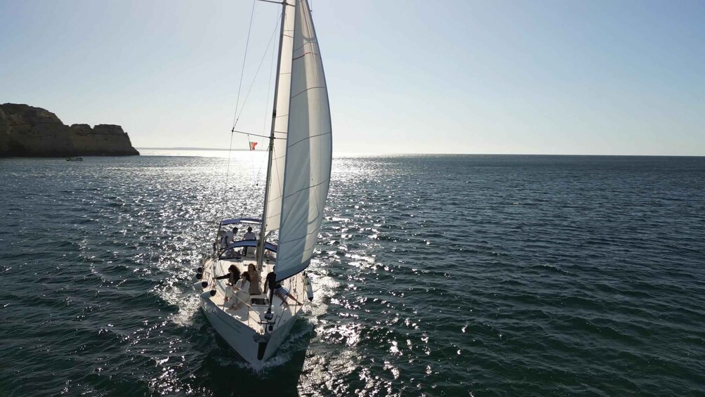 A sailboat on calm waters with a clear sky and distant cliffs. 2