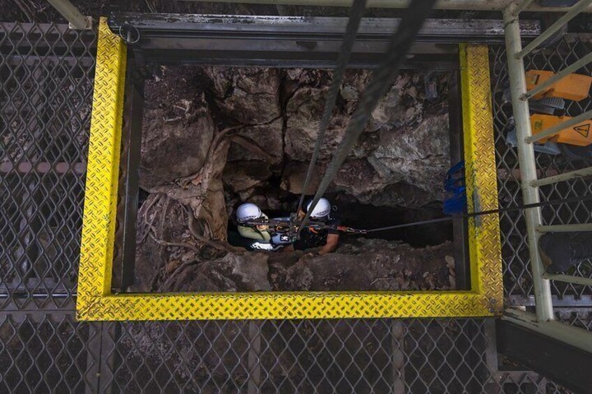 A person in a helmet and harness inside a metal frame with yellow diamond plate edges, working on a structure. 3