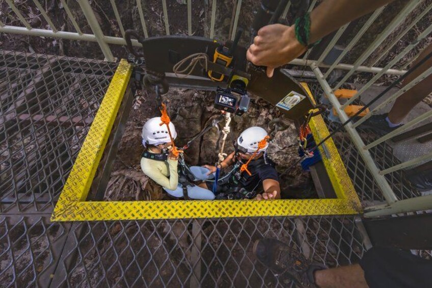 Two people in helmets and harnesses inside a metal cage with a yellow safety line. 2