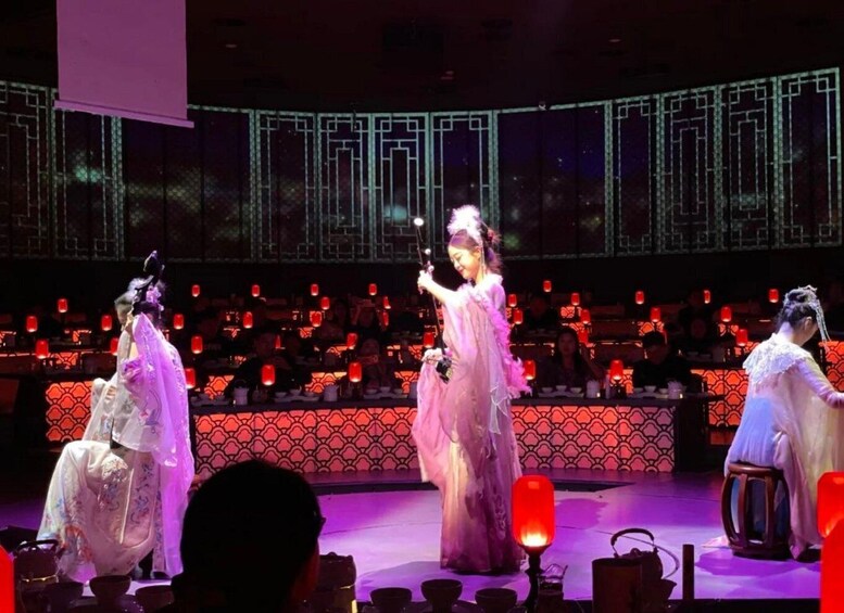 A stage performance with actors in traditional costumes, a seated audience, and a backdrop with geometric patterns. 4