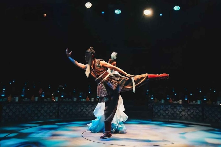 A dancer in mid-performance on a stage with a patterned backdrop and audience seating. 2