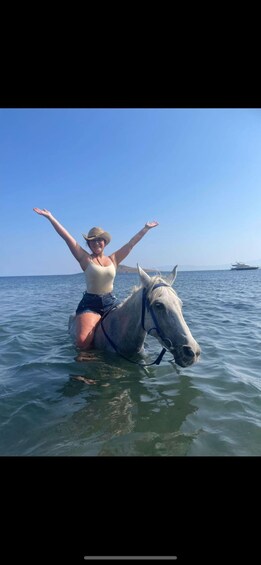 A person riding a horse in the water with arms raised. 1