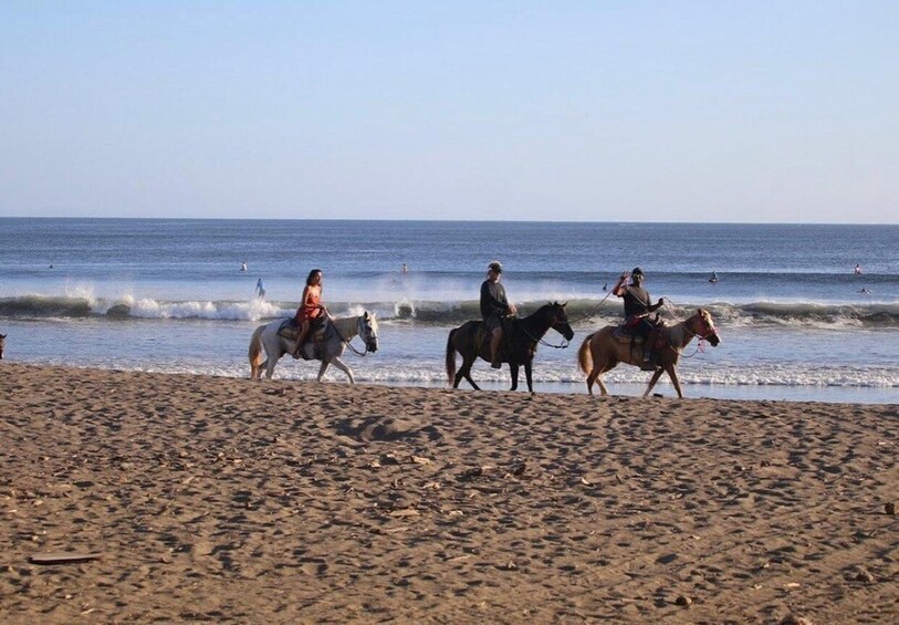 People riding horses along a beach with waves in the background. 2