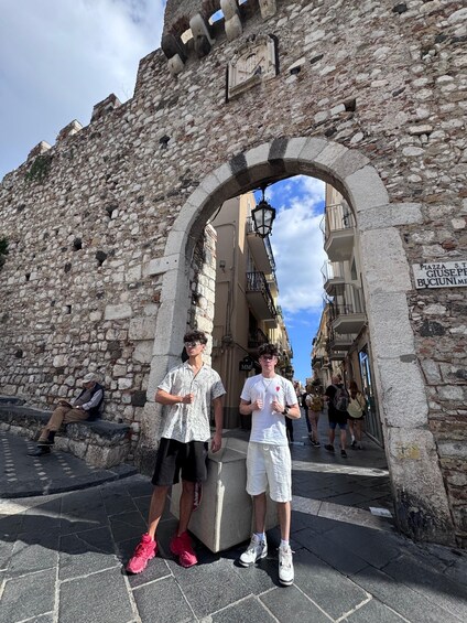 Two people standing in front of a stone archway with a sign reading 'Piazza St. Giuseppe Bucciuni.' 5