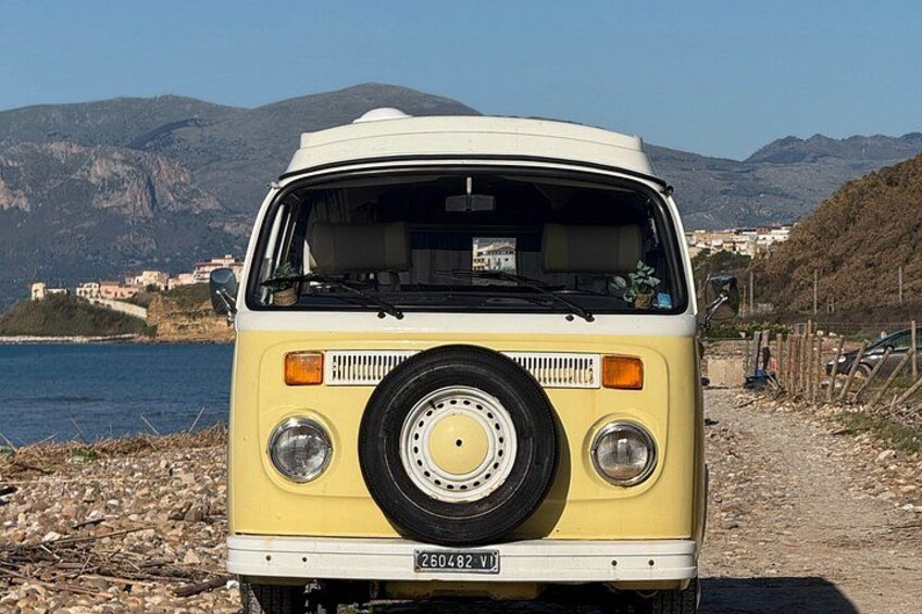 A yellow and white van parked by a rocky shore with a clear view of the sea and mountains in the background. 4