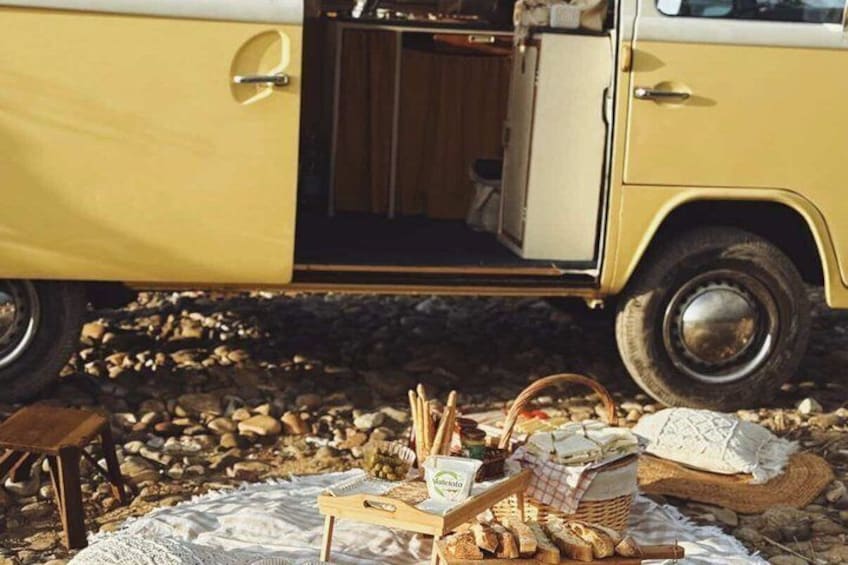 Un véhicule jaune, avec une porte ouverte, laissant entrevoir un espace cuisine, entouré d’objets d’extérieur tels que du pain, un panier et un tissu. 3