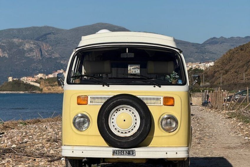 Un fourgon jaune et blanc est garé au bord d’une côte rocheuse, avec une chaîne de montagnes en arrière-plan. 4