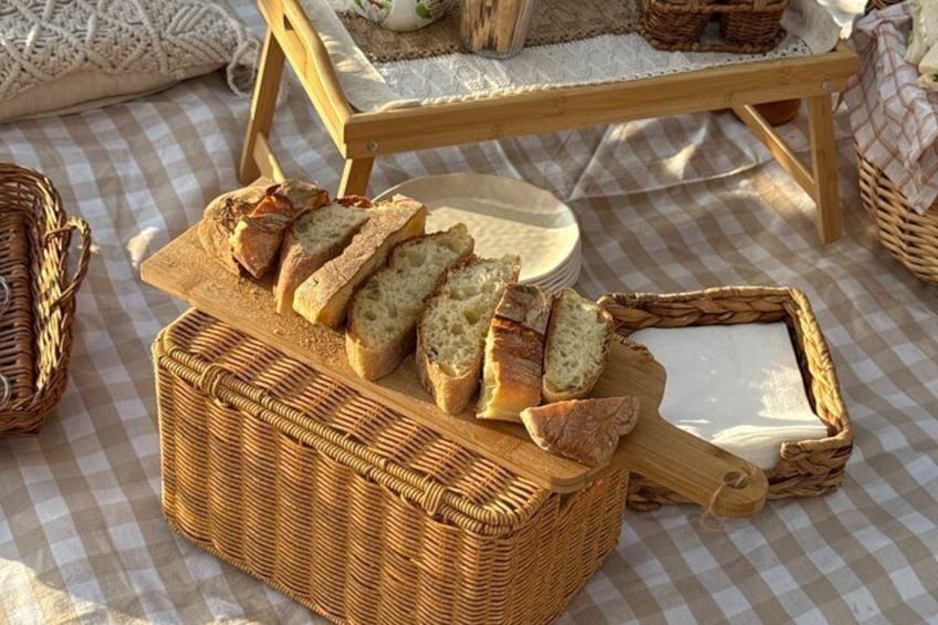 Un panier en osier contenant du pain tranché et une planche de fromages, le tout posé sur une nappe à carreaux. 5