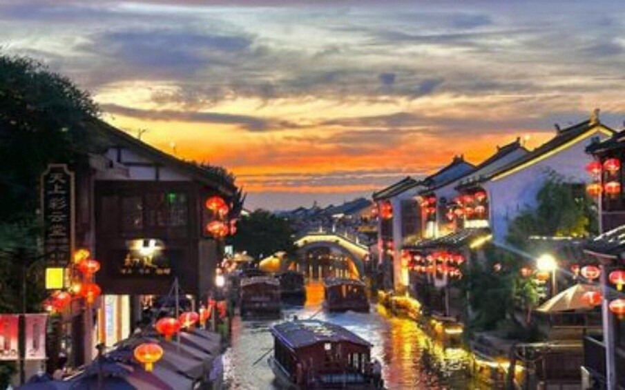 A traditional street at sunset with illuminated buildings and a boat on the water. 2