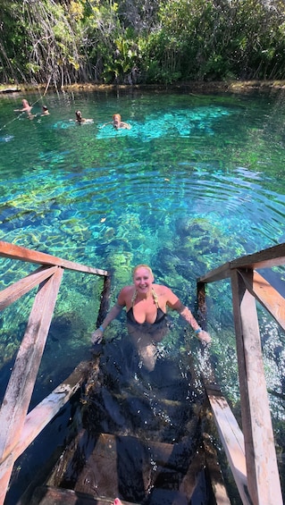 A person swimming in a clear blue pool with wooden steps leading into it. 4