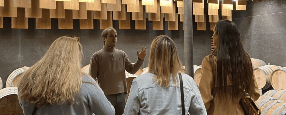 A group of people in a room with wooden panels on the wall and barrels in the background. 1