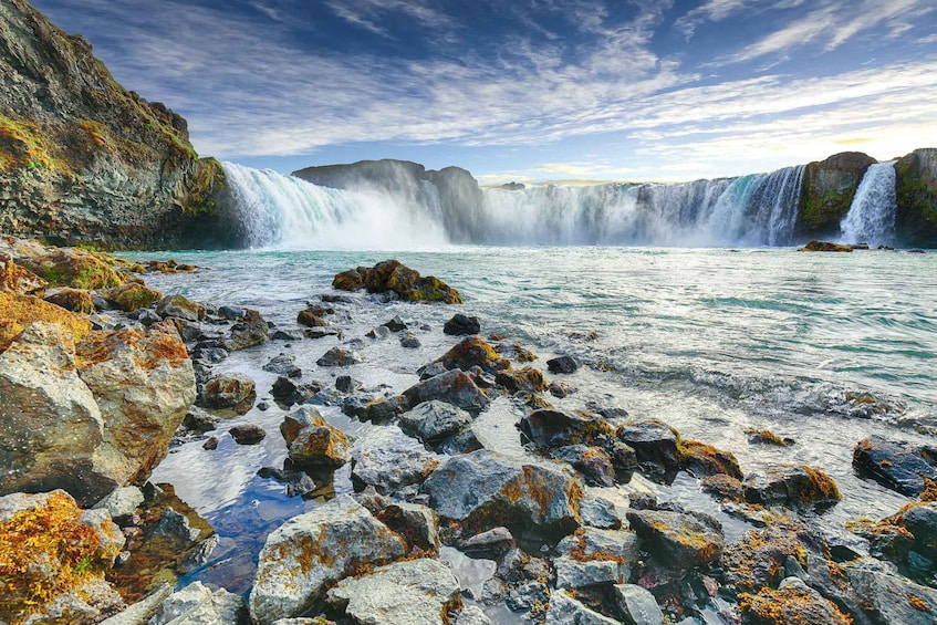 A waterfall cascading into a clear blue pool surrounded by rocky terrain with moss. 1