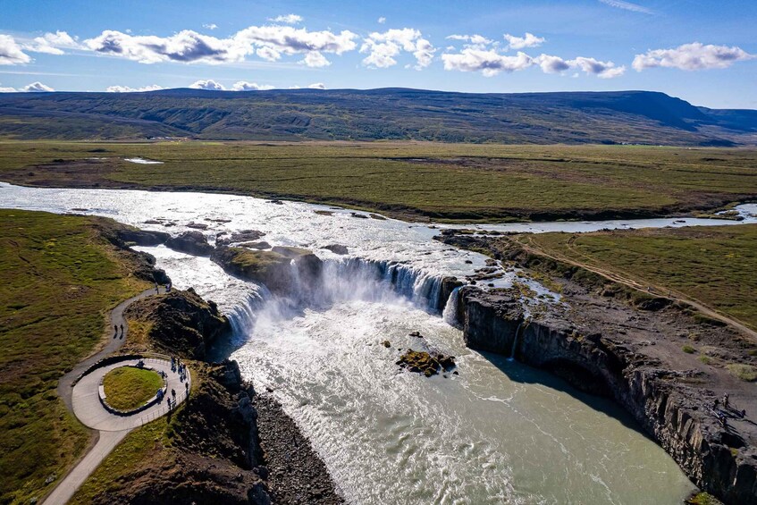 A waterfall cascading over a cliff, surrounded by a grassy landscape and a winding path. 3