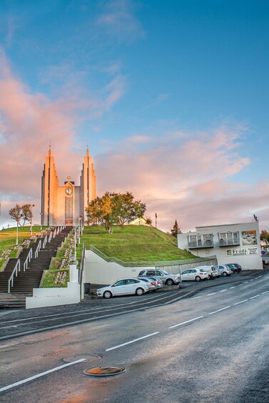 A church with a clock tower, a parking lot with cars, and a hill with trees. 5