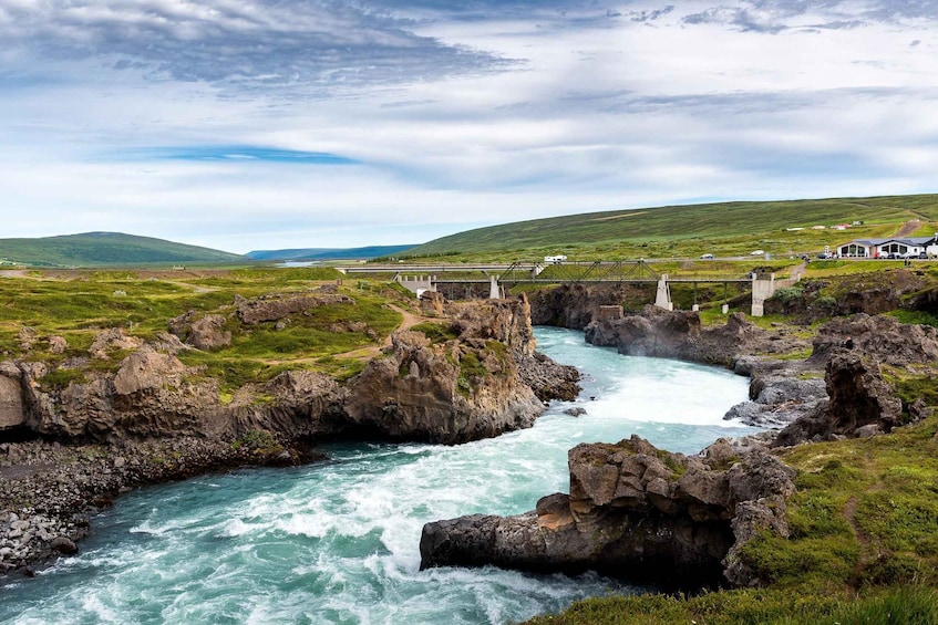 A river flowing through a rocky landscape with a bridge and buildings in the background. 2