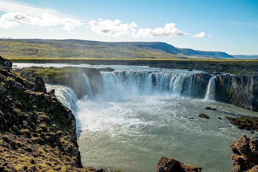 A waterfall cascading over a rocky cliff into a river, surrounded by a mountainous landscape. 4