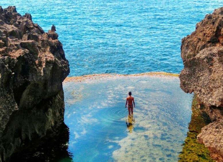 A person standing in clear water between rocky formations. 3