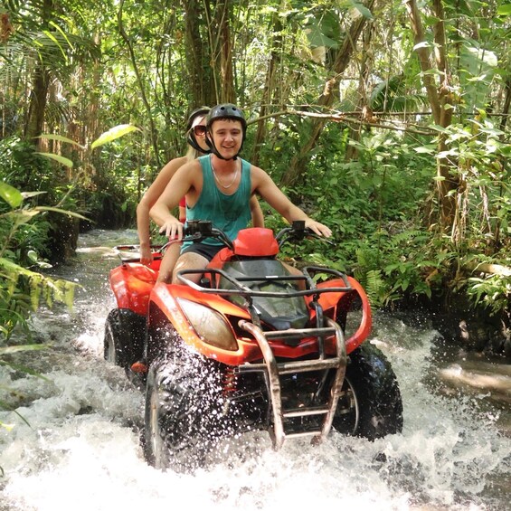 Two people on an ATV navigating through a water stream in a forested area. 3